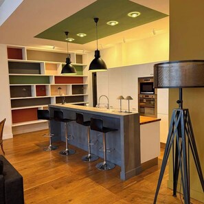 A modern kitchen with a bar area, wooden flooring, and a unique ceiling design.