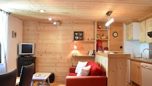 Un ambiente compatto con finiture in legno, un divano, una televisione, un piccolo tavolo da pranzo e un angolo cottura.