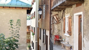 Una stretta via con edifici tradizionali, un balcone in legno e una sedia rossa davanti a un palazzo.