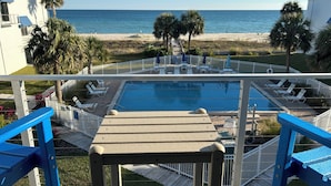 A pool area with a view of the beach, lounge chairs, and palm trees. - SEASHELL ESCAPE - Pool & Beach Front 2 Bedroom sleeps 6 - Enjoy!!! (St. George Island)
