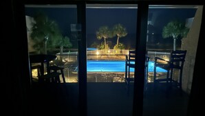 A view of a swimming pool at night with surrounding palm trees and a fence. - SEASHELL ESCAPE - Pool & Beach Front 2 Bedroom sleeps 6 - Enjoy!!! (St. George Island)