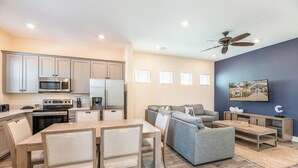 A modern kitchen with built-in appliances, a dining area with a wooden table and chairs, a gray sofa, and a ceiling fan. - Sunrise Cottage near Disney with Margaritaville Resort & Island H20 Waterpark. (Kissimmee)