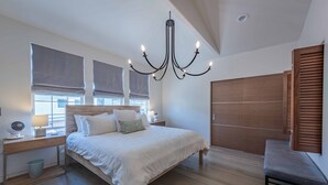 A bedroom with a large bed, bedside tables, a wooden wardrobe, and a chandelier. - Luxe Designer Condo w/BBQ, Gourmet Kitchen & ½ Block to the Beach in Avila! (Avila Beach, CA)