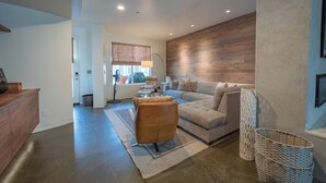 A modern living room with a large sectional sofa, a coffee table, and a wooden accent wall. - Luxe Designer Condo w/BBQ, Gourmet Kitchen & ½ Block to the Beach in Avila! (Avila Beach, CA)