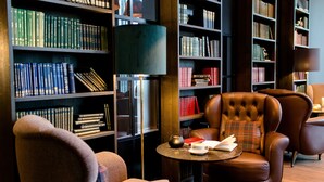 Una biblioteca amb butaques de pell, una taula rodona amb llibres i una teiera, i altes estanteries plenes de llibres.