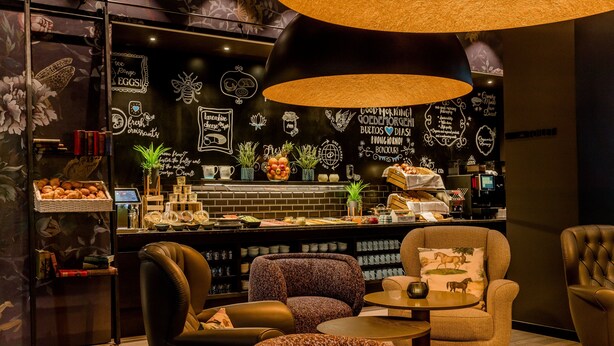 Zona de bar acollidora amb seients, una barra amb menjar i begudes, i decoració mural.