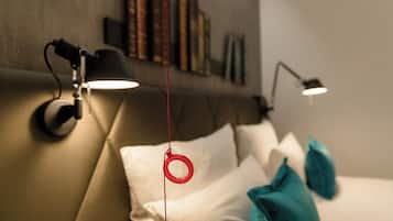 Un dormitorio con cama, almohadas, un objeto rojo colgante y dos lámparas fijadas a la pared.
