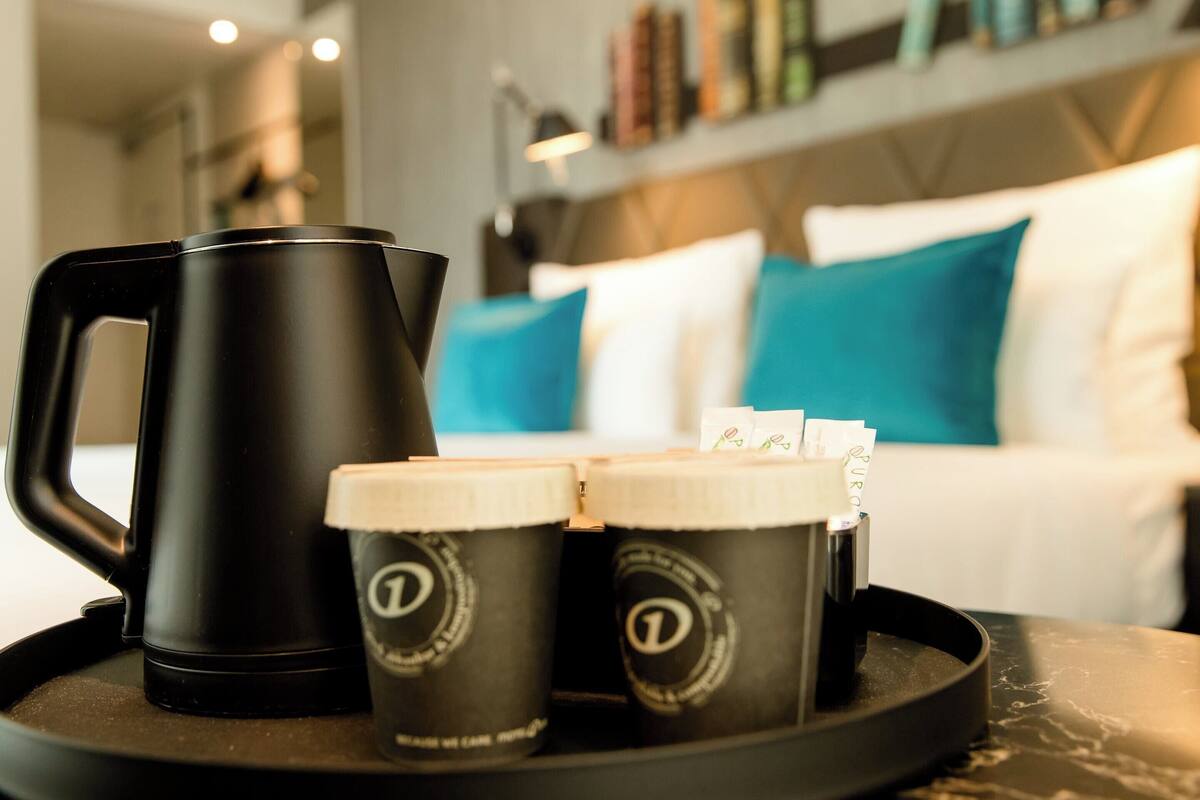 A black coffee maker and two coffee cups with lids on a tray.