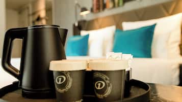A black coffee maker and two coffee cups with lids on a tray.