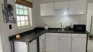 A modern kitchen with a black countertop, white cabinets, a built-in microwave, and a window with blinds. - Modern & Private Sun Valley getaway for two (Sun Valley)