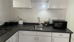 A modern kitchen with white cabinets, a black countertop, a stainless steel sink, a kettle, a microwave, and a small cactus plant. - Modern & Private Sun Valley getaway for two (Sun Valley)