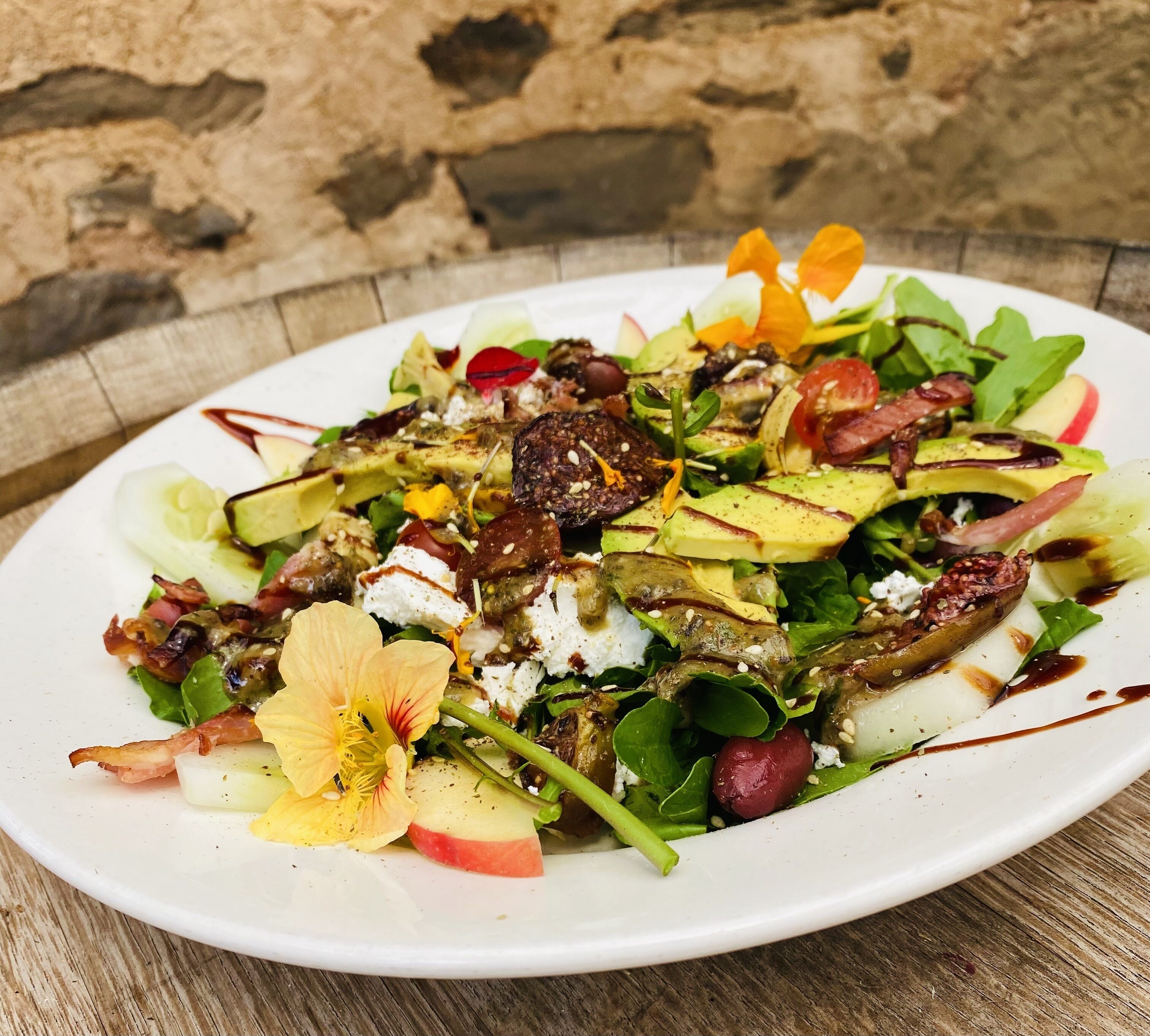 A white plate with a salad on a wooden table.