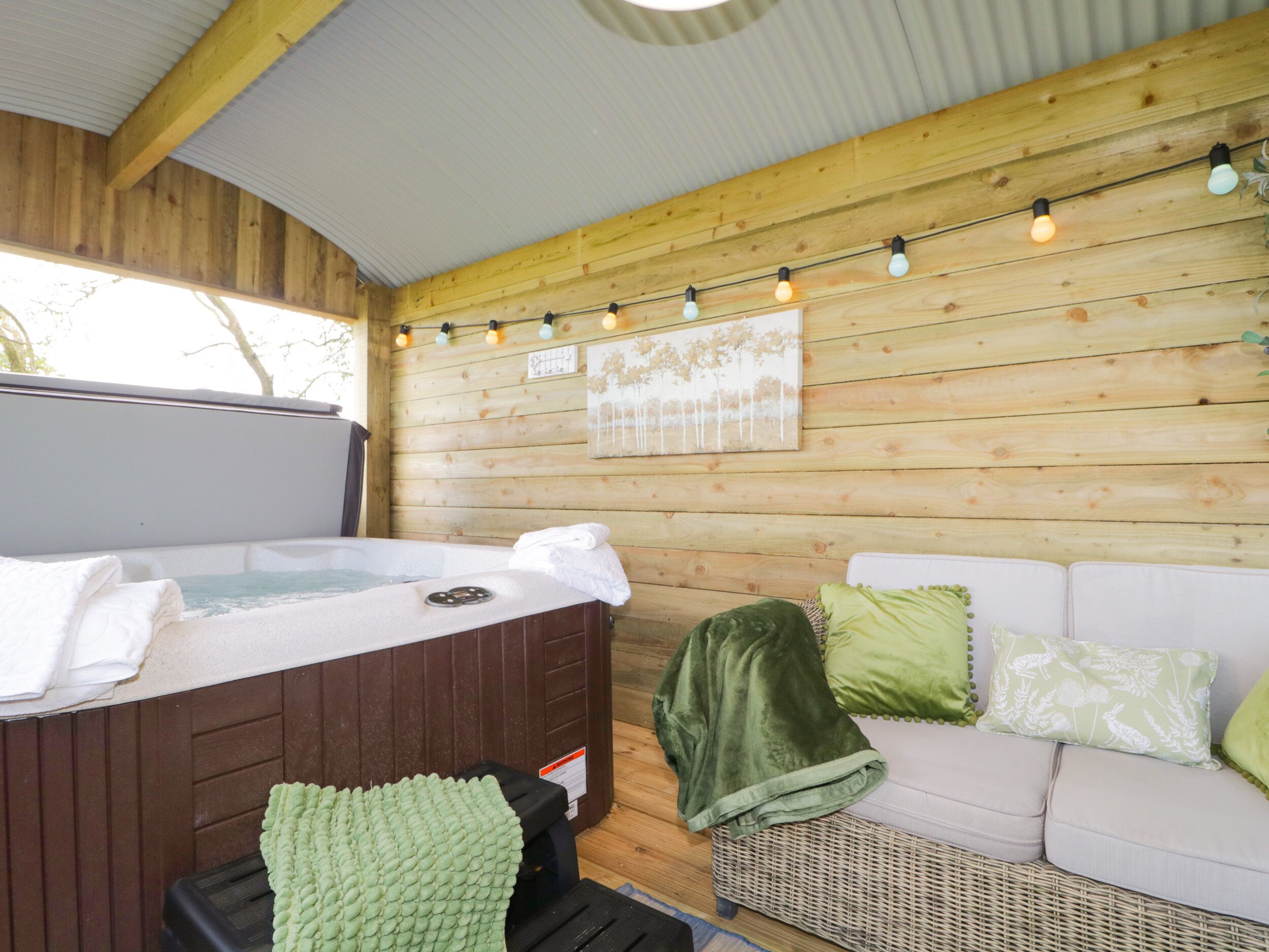 A wooden cabin interior with a hot tub, a white sofa, and string lights.