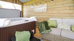 A wooden cabin interior with a hot tub, a white sofa, and string lights. - High Rigg Shepherd's Sunset (Brampton)