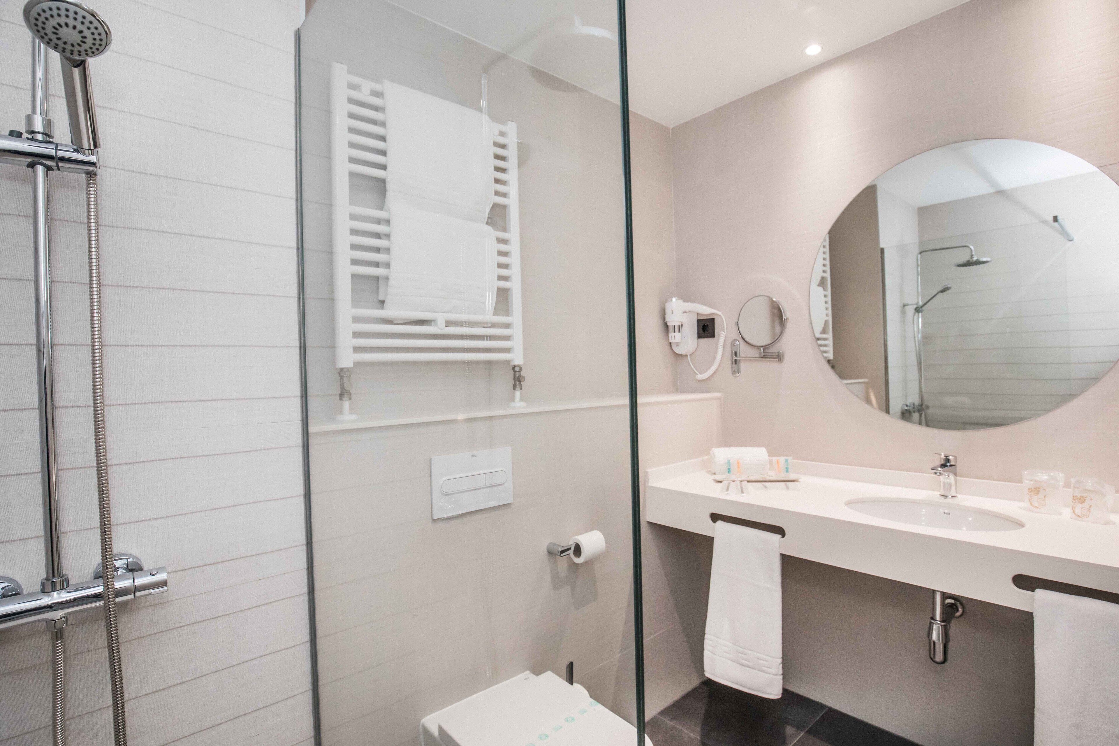Un baño moderno con ducha de vidrio, un lavamanos blanco y un espejo grande.