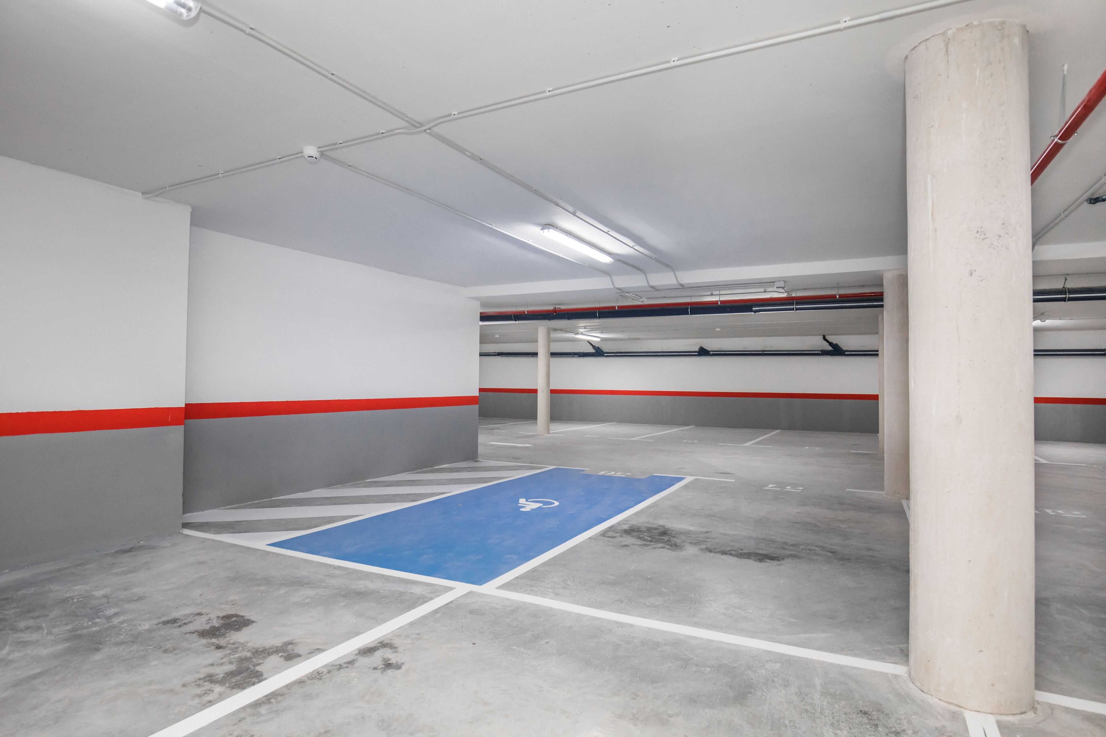 Un aparcament interior amb sòls de formigó, parets blanques i detalls vermells.