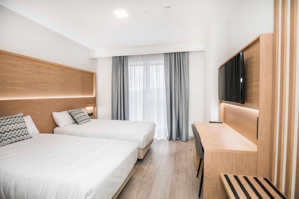 A modern hotel room with two beds, a desk, and a TV.