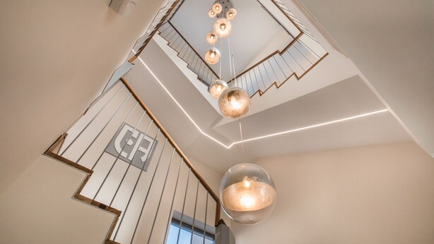 Een modern interieur met een trap, een kroonluchter en een geometrisch plafondontwerp.