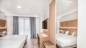 Een moderne hotelkamer met twee bedden, een bureau, een televisie en een groot raam met gordijnen.