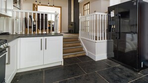 A modern kitchen with white cabinetry, a black refrigerator, and a staircase leading to another level. - Fellside Lodge (Windermere)