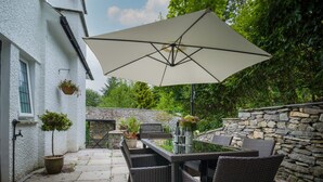 A patio with wicker furniture, a table, and an umbrella. - Fellside Lodge (Windermere)