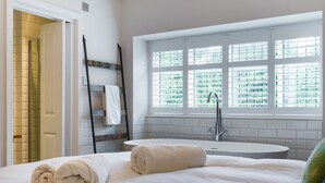 A hotel room with a bed, a window with blinds, a bathtub, and a towel rack. - Fellside Lodge (Windermere)