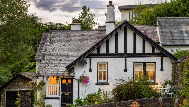 A traditional half-timbered house with a stone facade, a black door, and a small garden with a stone wall and a lantern. - Fellside Lodge (Windermere)