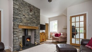 A cozy living room with a stone fireplace, leather sofas, and a wooden cabinet. - Fellside Lodge (Windermere)