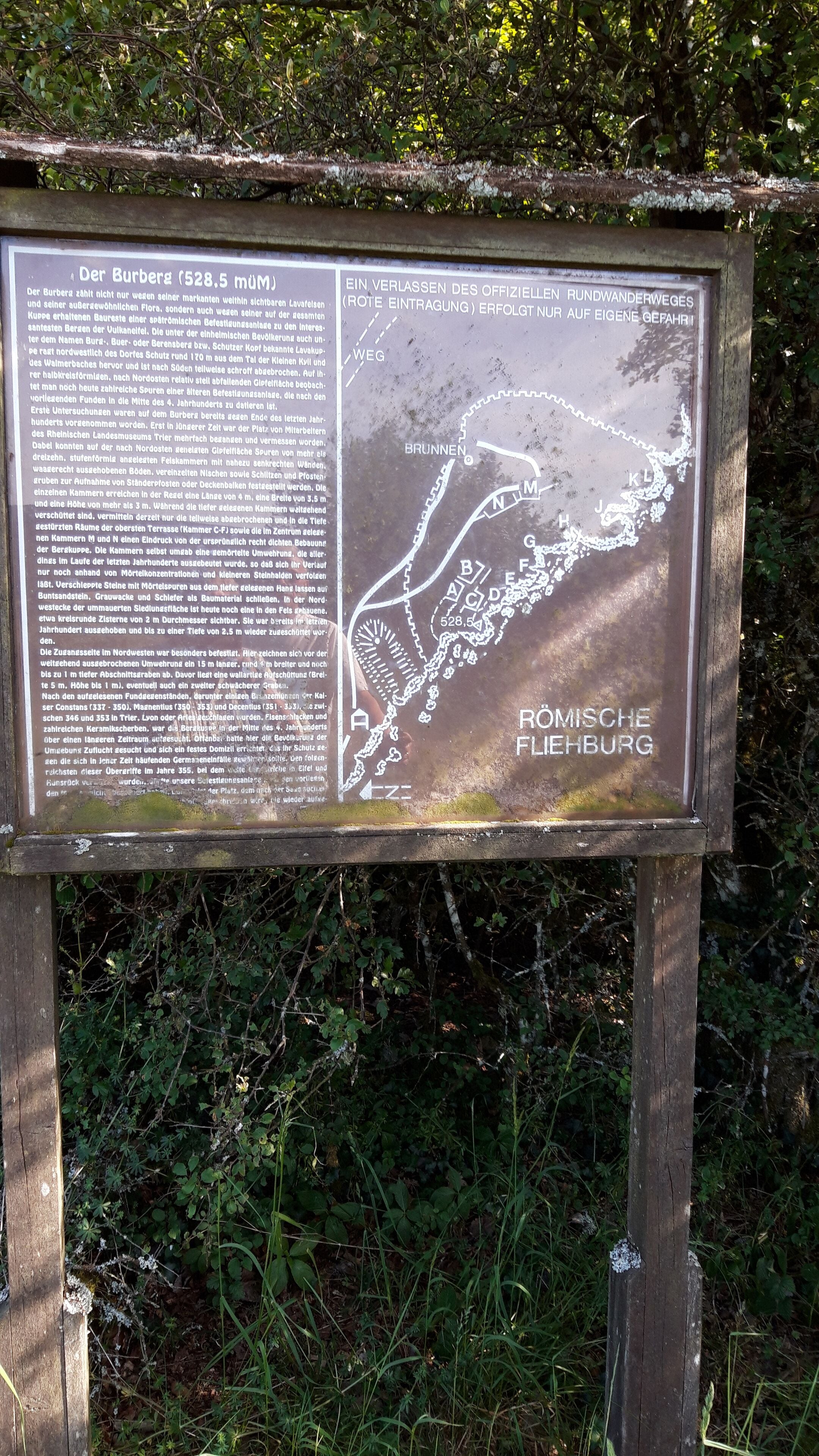 A signboard with text and a map, likely providing information about a hiking trail or historical site.