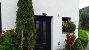Een wit gebouw met een zwarte deur, planten in potten en een klein raam met gele bloemen.