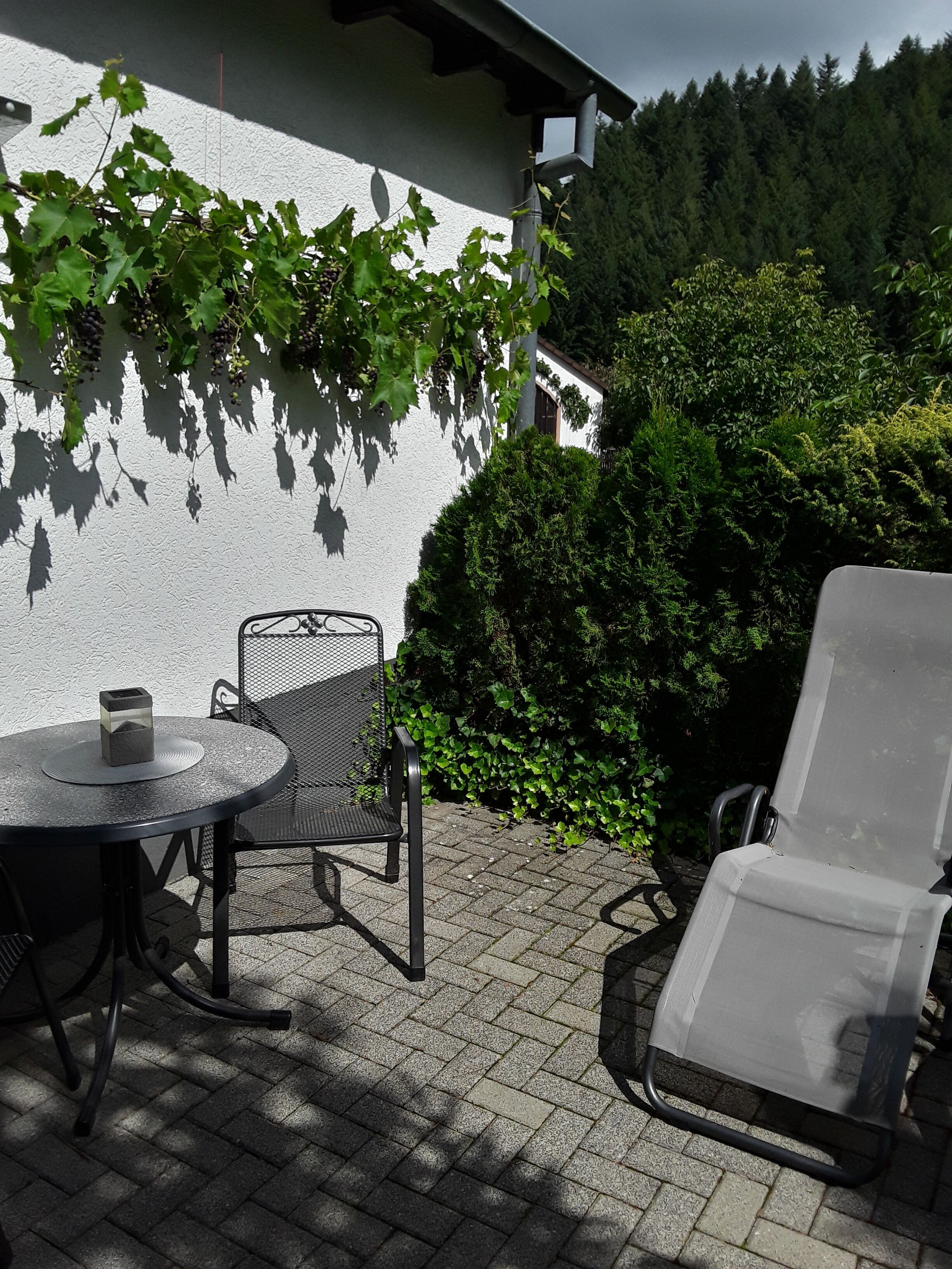 Eine Terrasse im Freien mit einem runden Tisch, zwei Stühlen und einer Liege.