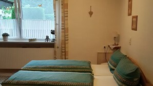 Een slaapkamer met een houten bed, nachtkastje, lamp en raam met gordijnen.