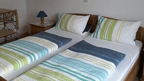 A double bed with striped bedding, a bedside table with a lamp, a framed picture on the wall, and a wooden headboard. - Vacation apartment Hunz - Apartment 2 (Schutz)