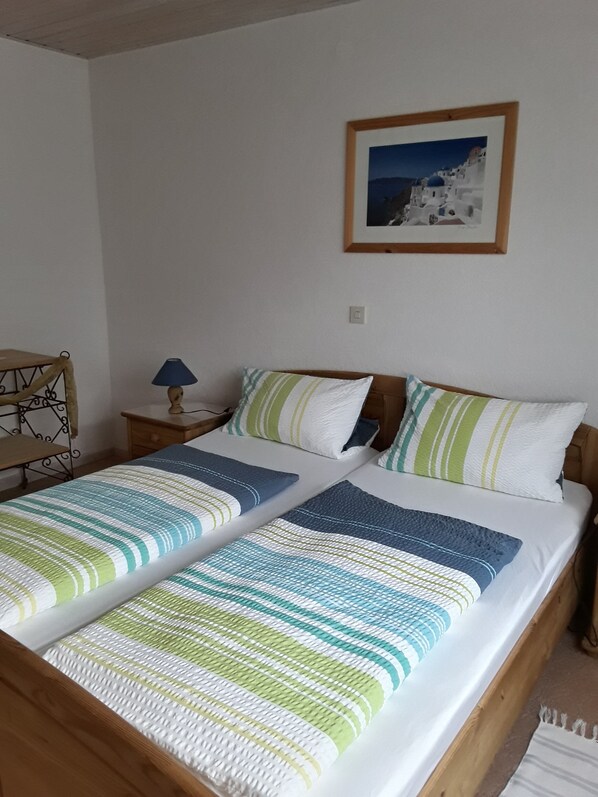Ein Doppelbett mit gestreifter Bettwäsche, ein Nachttisch mit Lampe, ein gerahmtes Bild an der Wand und ein Holz-Kopfstück.
