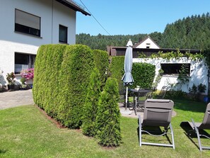 Un jardin bien entretenu, avec une haie soigneusement taillée, du mobilier d’extérieur et un espace patio.