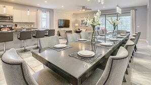 Uma  área de refeições moderna com uma mesa comprida, cadeiras e uma televisão ao fundo.