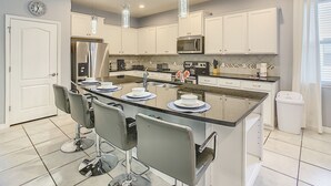 Cozinha moderna com armários brancos, eletrodomésticos de aço inoxidável e uma ilha central com banquetas.