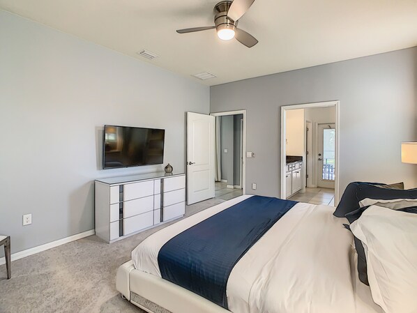 A bedroom with a bed, a TV, a dresser, and a ceiling fan.
