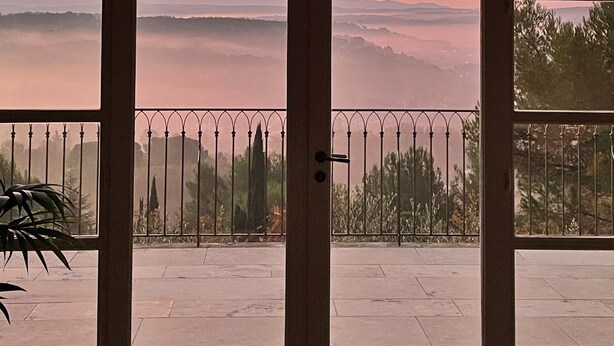 A view through a large arched window with a metal railing, overlooking a landscape with distant mountains and a sunset. - Panoramic 4-BR Villa near Aix w/Pool, AC - for 10 people (Le Tholonet (13100))