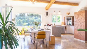 A modern kitchen with a large island, wooden beams, and a view of greenery outside.