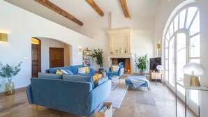 A spacious living room with a large blue sofa, a fireplace, and a large arched window. - Panoramic 4-BR Villa near Aix w/Pool, AC - for 10 people (Le Tholonet (13100))
