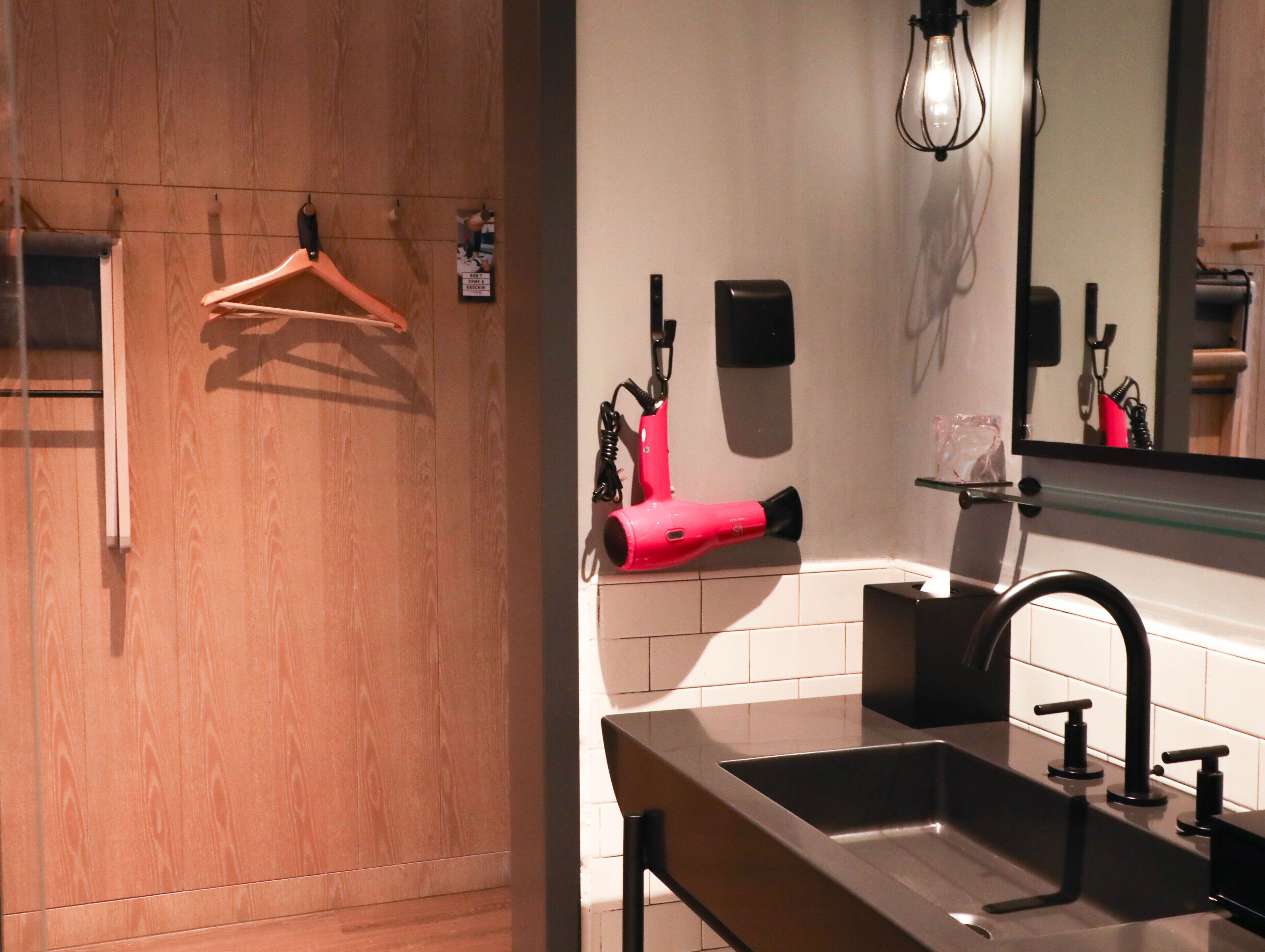 A bathroom with a wooden panel wall, a black sink, a mirror, and a red hairdryer.
