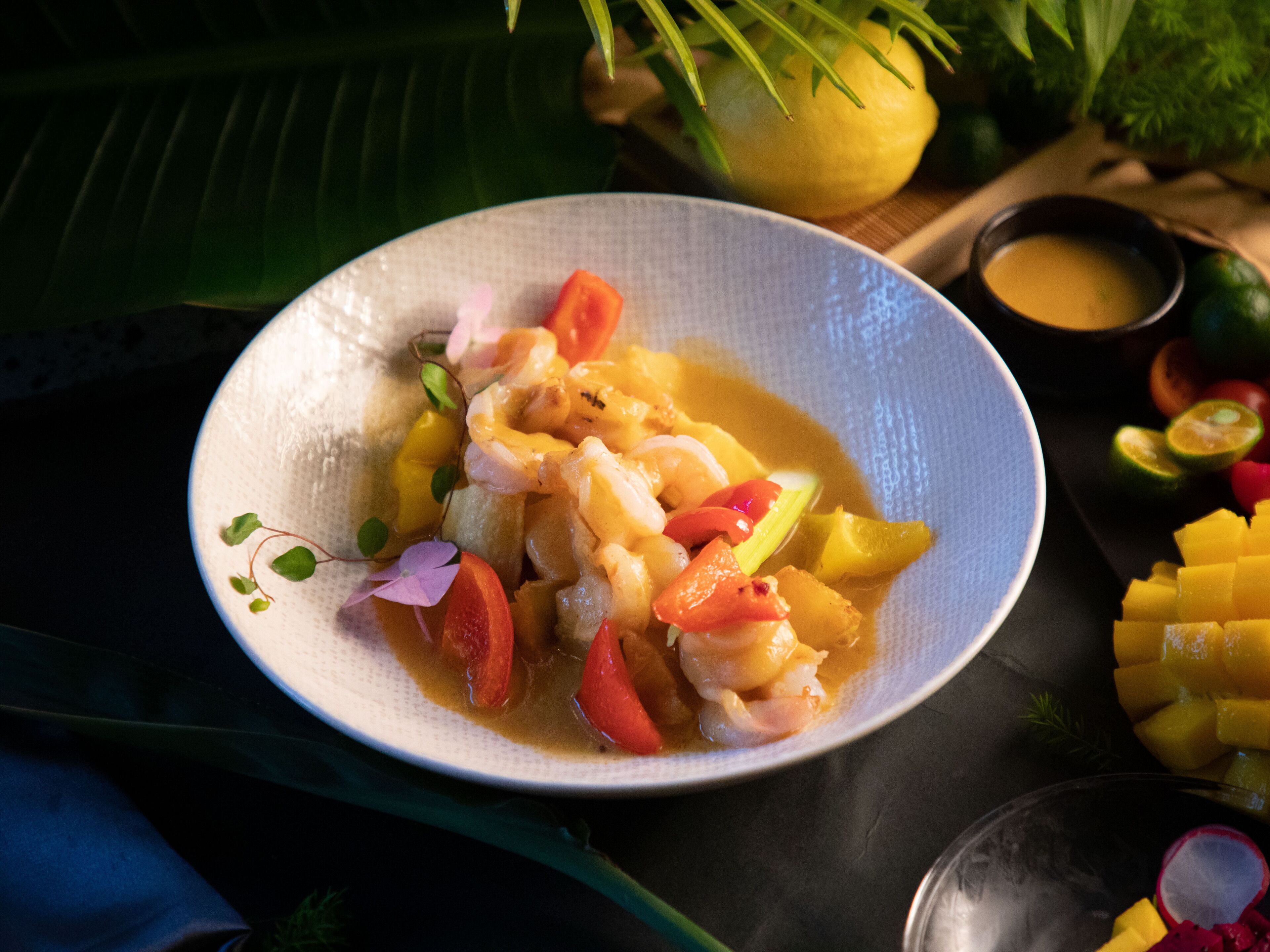 A plate of seafood with vegetables and a small bowl of sauce.