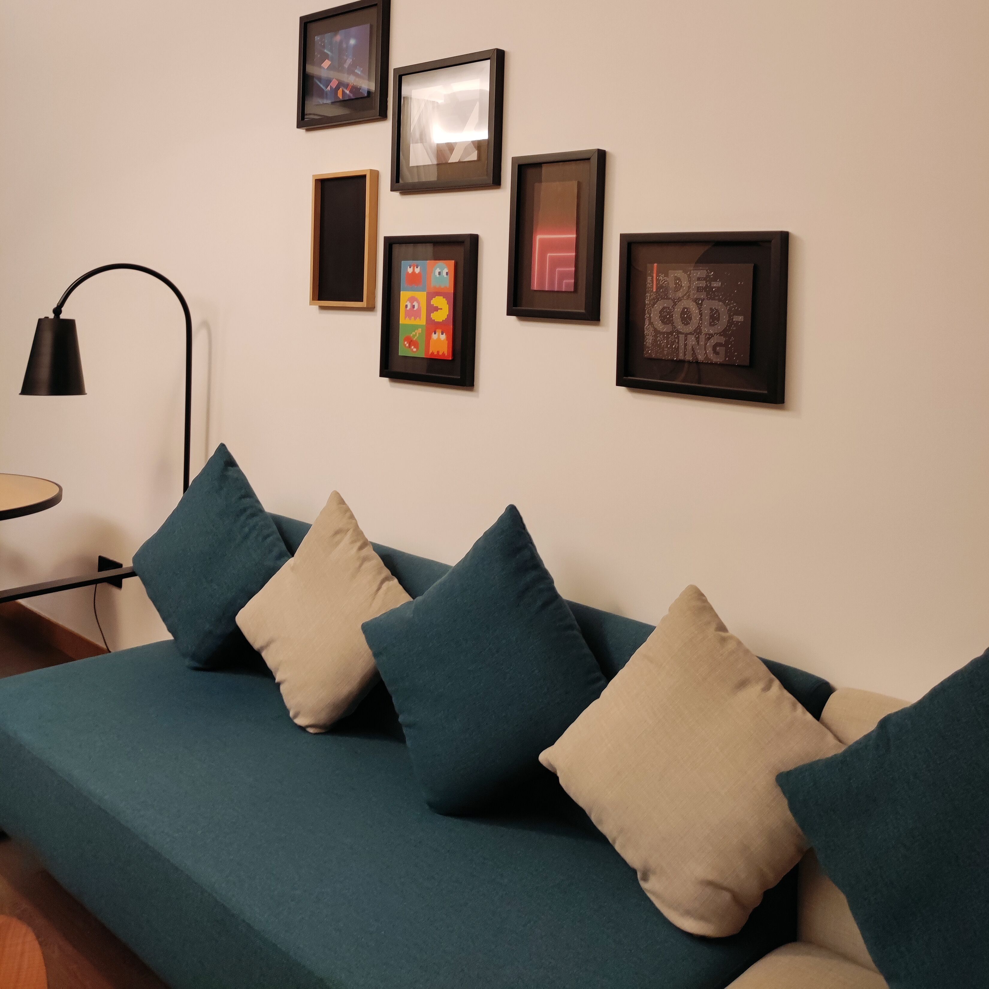A modern living room with a teal sofa, multiple framed artworks, and a floor lamp.