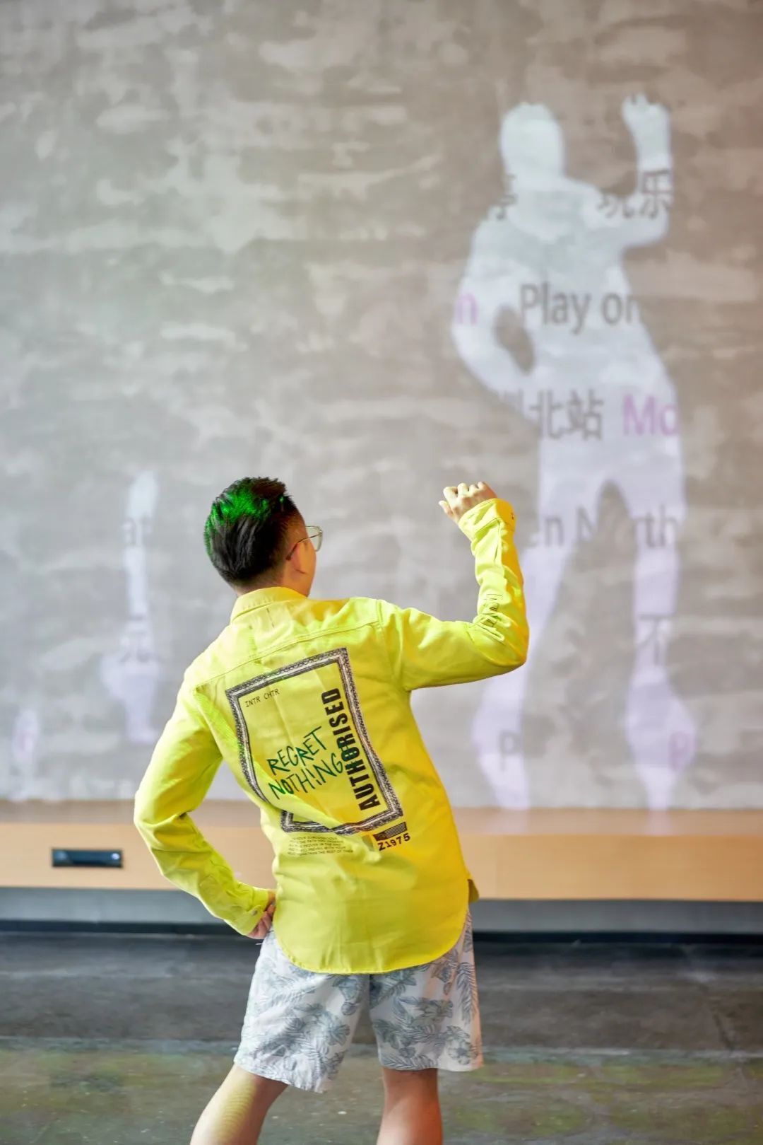 A person in a yellow shirt with a back label reading "REJECT NOTHING AUTHORIZED" standing in front of a projection screen displaying a silhouette of a person playing a sport.