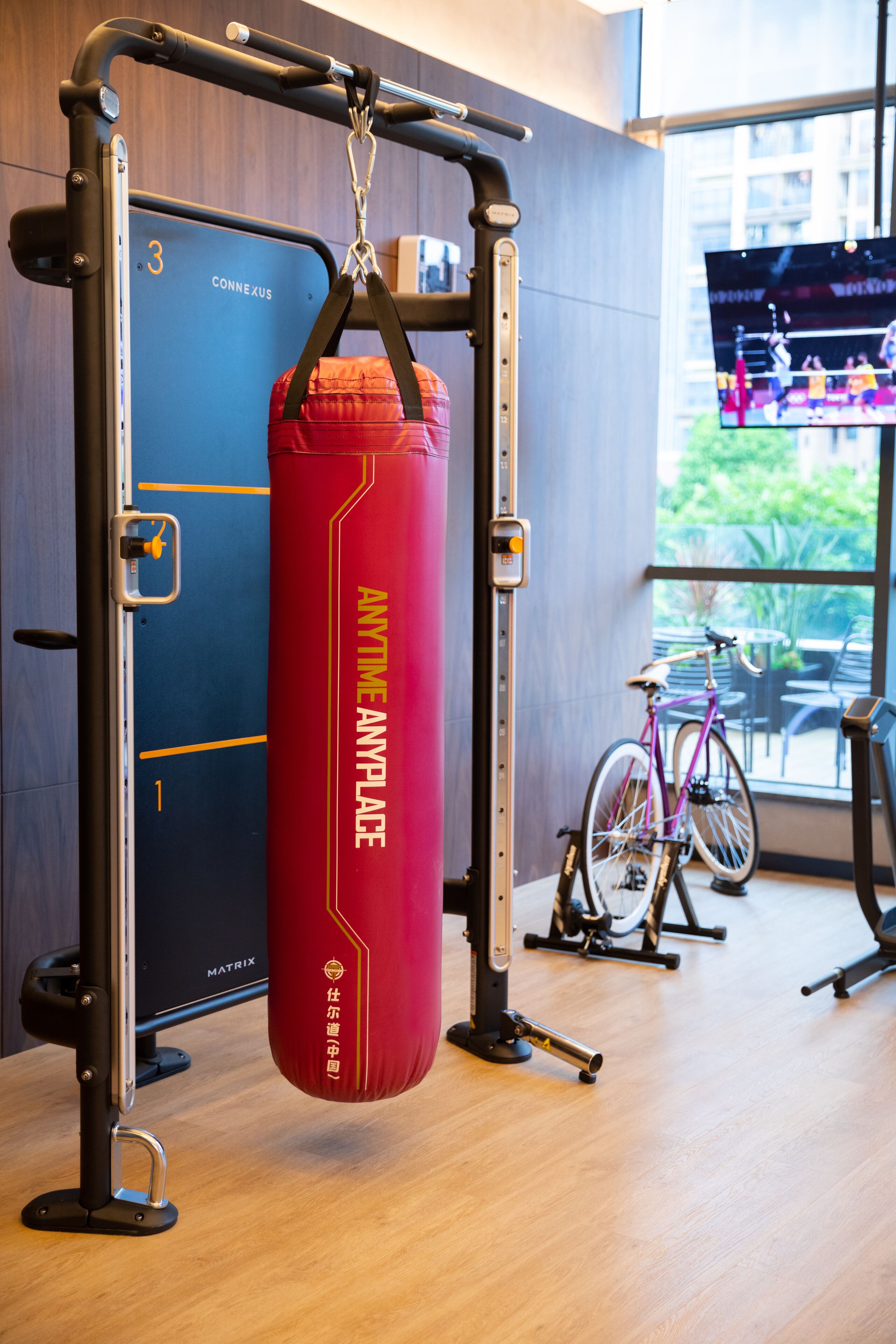 A gym with a punching bag, a bicycle, and a television displaying a sports event.