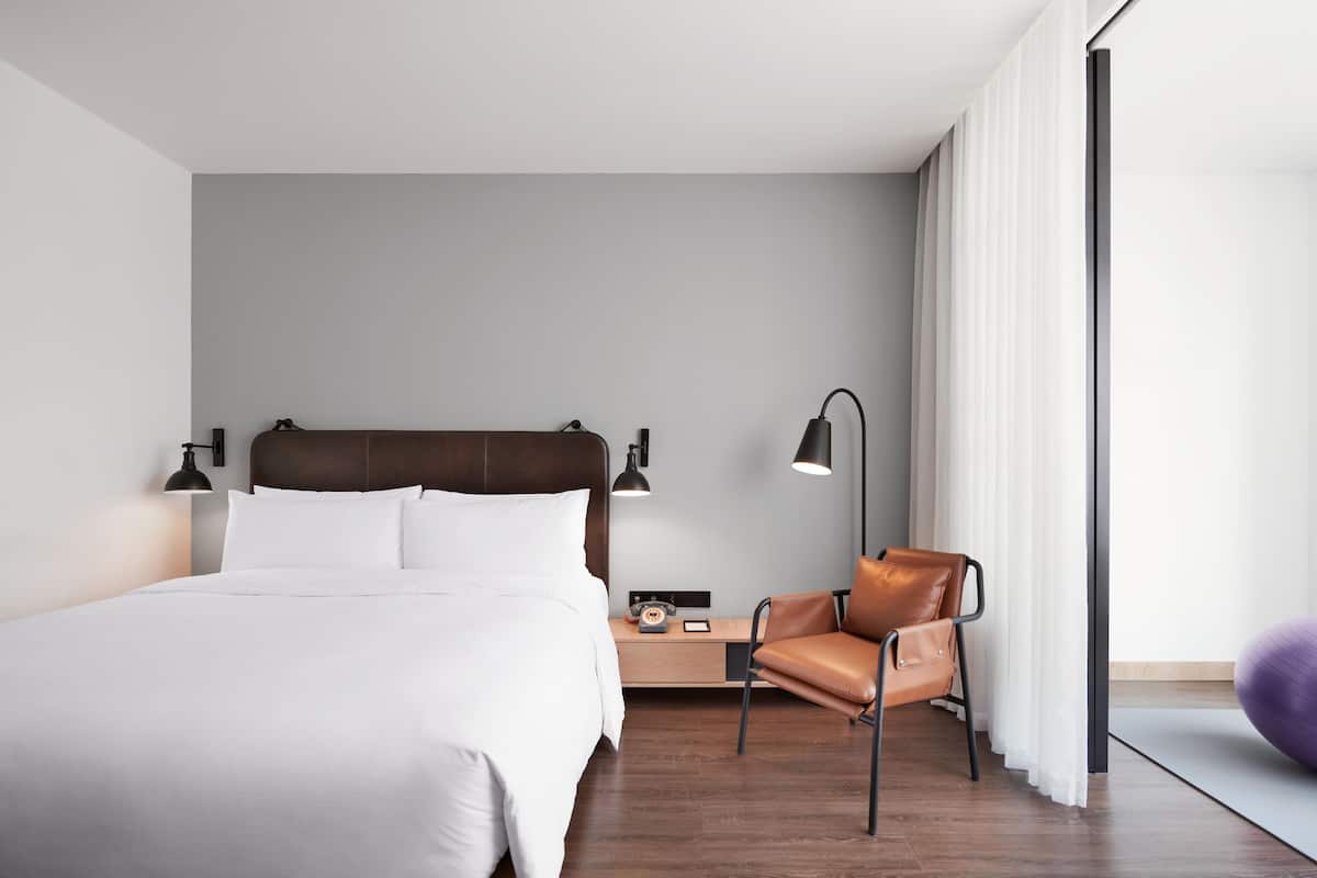 Moderni hotellihuone, jossa on suuri sänky, työpöytä lampun kanssa, nahkainen tuoli ja näkymä ulos.