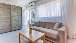 A modern living room with a sofa, a wooden coffee table, and a view through a large window with sheer curtains. - SUEDE 4 - balcon & clim, à 100 m plage - By Rivier (Niza)