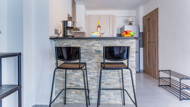 A modern kitchen with two bar stools, a coffee maker, and a fruit bowl. - SUEDE 4 - balcon & clim, à 100 m plage - By Rivier (Niza)