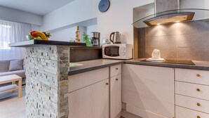 A modern kitchen with a stone accent wall, a microwave, a kettle, and a clock on the wall. - SUEDE 4 - balcon & clim, à 100 m plage - By Rivier (Niza)